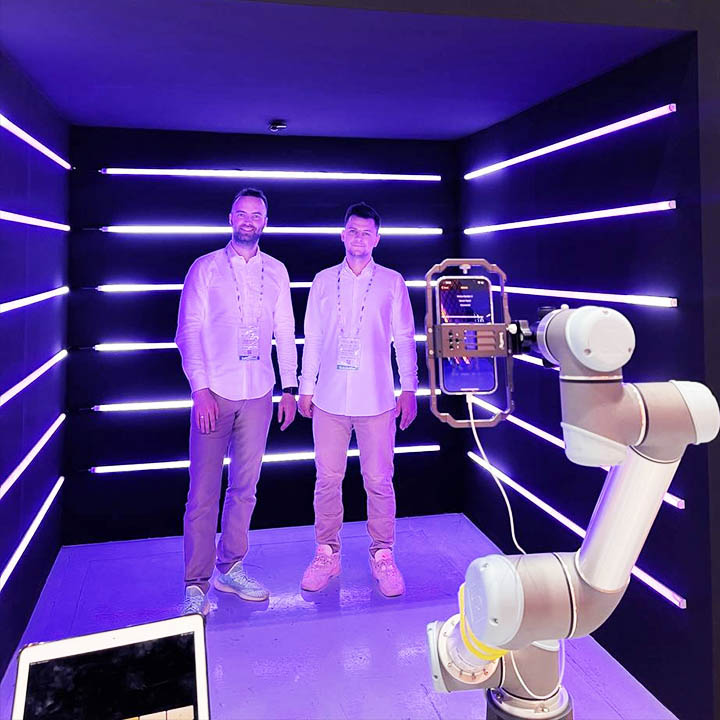 Two men are making a video in Neon Cube Photobooth. Robotic arm is equipped with camera and moves according to the pre-made programme.