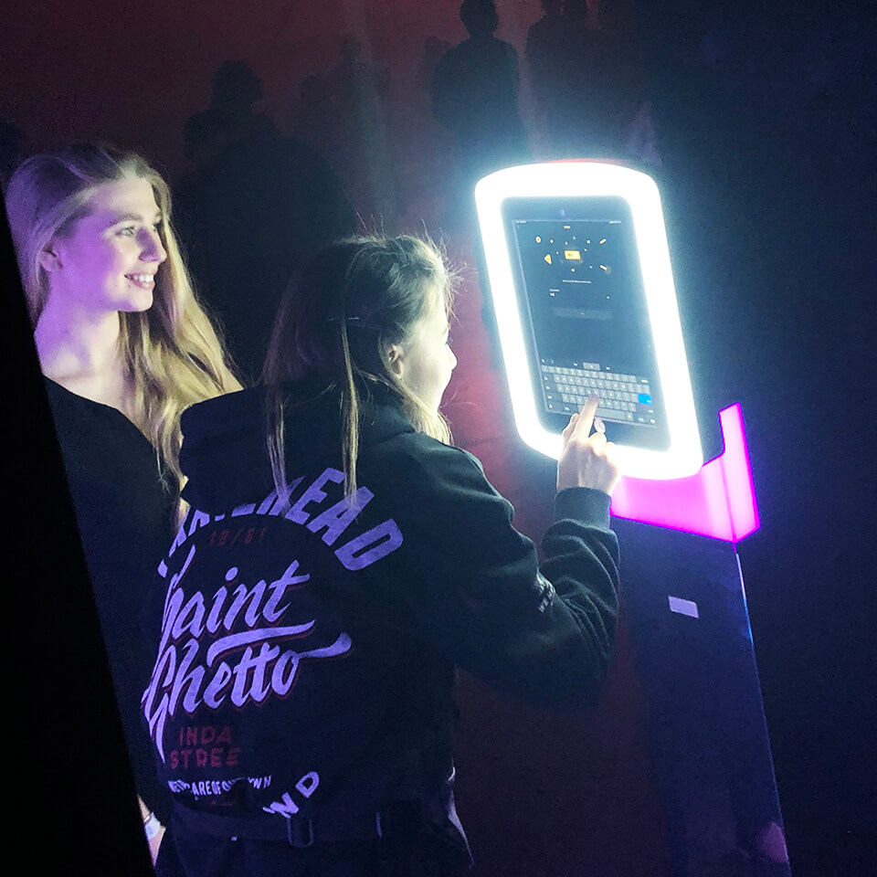 Two ladies laughing and posing in a photo booth with bright neon white light