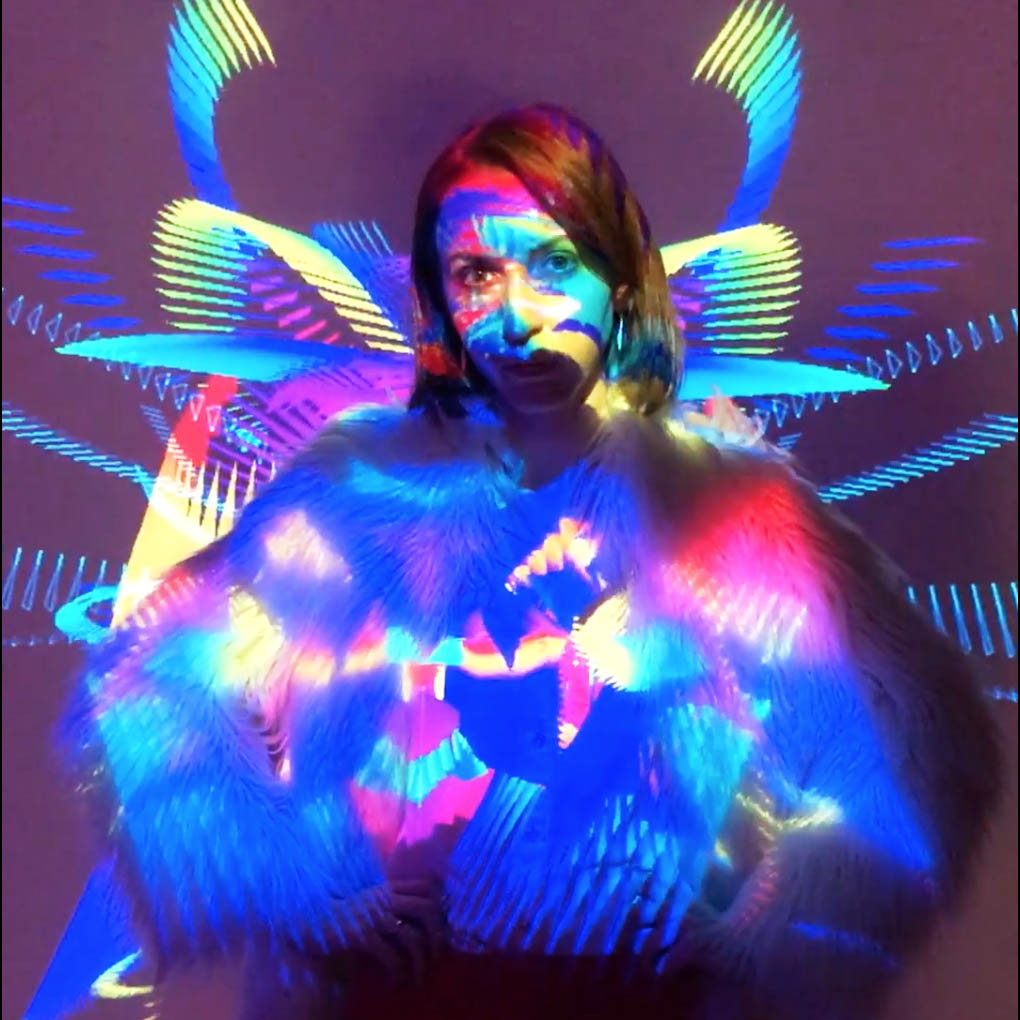 Lady is making a video for social media in Projection Cube Photobooth. Bright colourful shapes are projected on her.