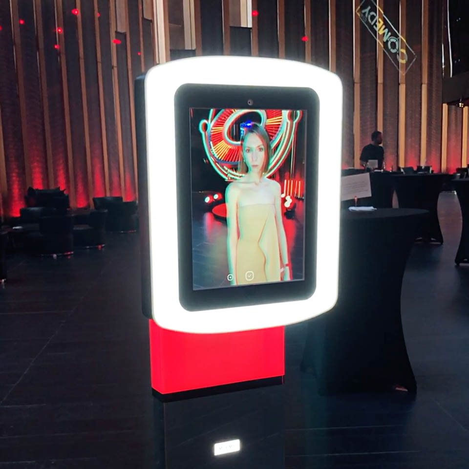 Lady is using Mixme Photo booth on an event. The booth with red decorative backlight is recording video.